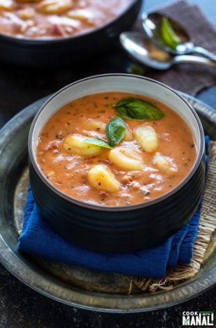 tomato gnocchi soup in a black bowl garnished with basil and some spoons in the background