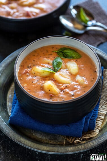 tomato gnocchi soup in a black bowl garnished with basil and some spoons in the background