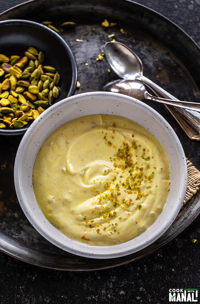 shrikhand in a bowl garnished with pistachios and bowl of pistachios in the background