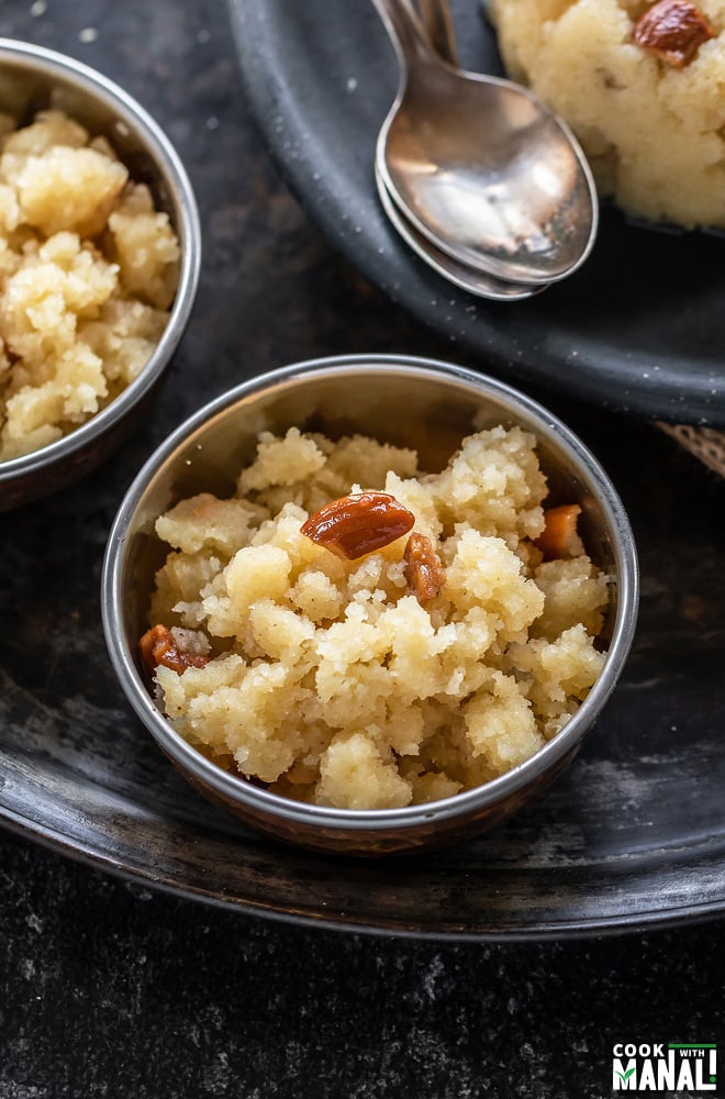 sooji halwa served in a small copper bowl with one more bowl and spoons in the background