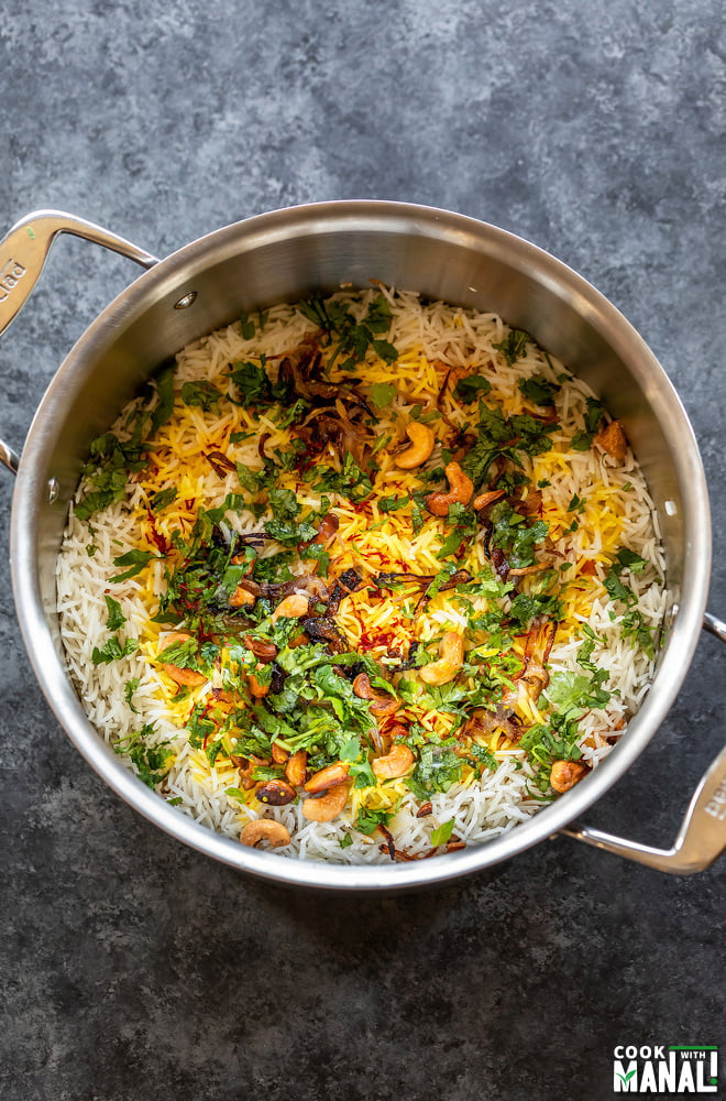 a large steel pot with layers of rice, veggies, herbs, caramelized onion and nuts and saffron