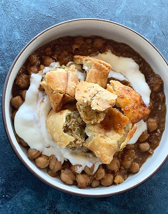 samosa on top of chole and yogurt in a bowl