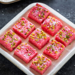 9 pieces of coconut rose kalakand placed in a plate and garnished with pistachios