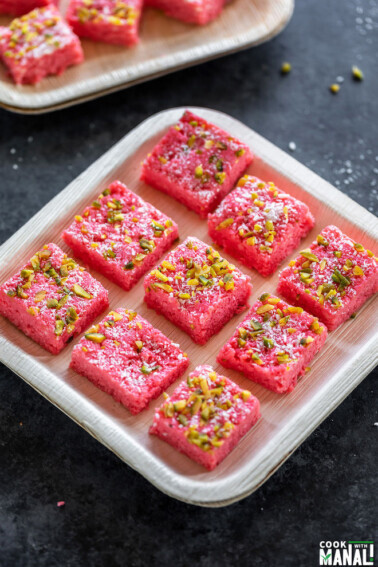 9 pieces of coconut rose kalakand placed in a plate and garnished with pistachios