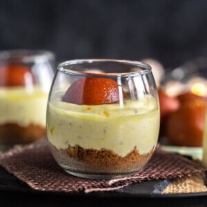 gulab jamun shrikhand jars placed on brown piece of cloth with gulab jamuns in the background