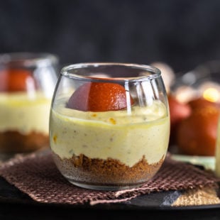 gulab jamun shrikhand jars placed on brown piece of cloth with gulab jamuns in the background
