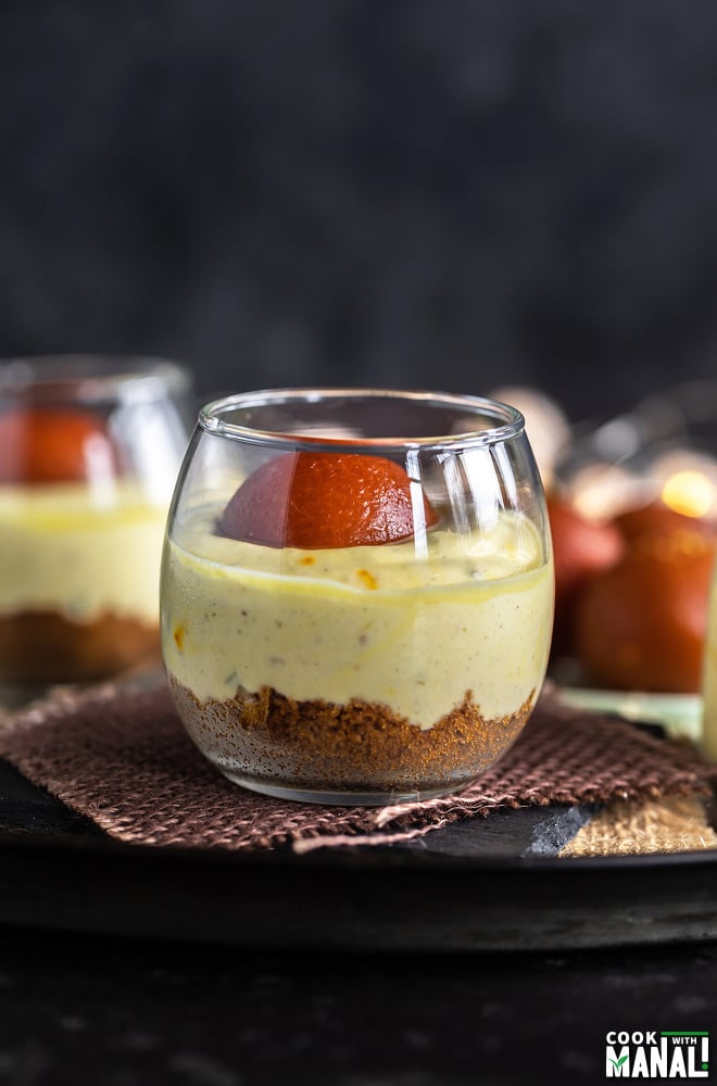 gulab jamun shrikhand jars placed on brown piece of cloth with gulab jamuns in the background