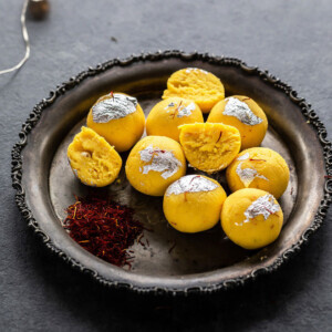 kesar malai ladoo on a silver plate with saffron strands placed on the side