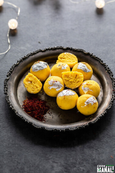 kesar malai ladoo on a silver plate with saffron strands placed on the side
