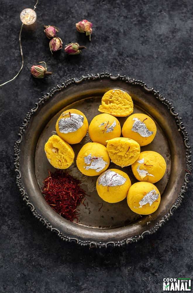 overhead shot of kesar malai ladoo arranged on a silver plate with saffron strands placed on the sides