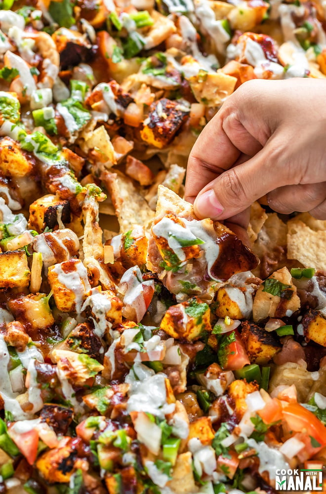 hand scooping out a paneer nachos from a sheet full of nachos
