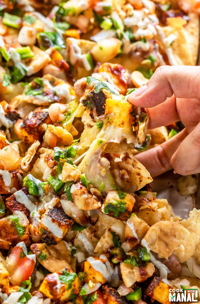hand pulling a paneer nachos loaded with cheese