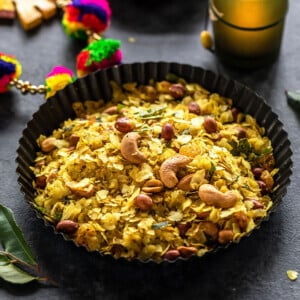 roasted poha chivda served in black rimmed plate with a candle lit in the background and some curry leaves on the side