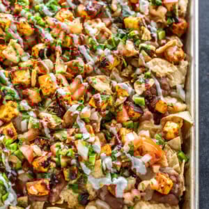 a full sheet of nachos topped with paneer, cheese, onion, tomato, cilantro