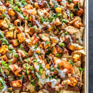 a full sheet of nachos topped with paneer, cheese, onion, tomato, cilantro