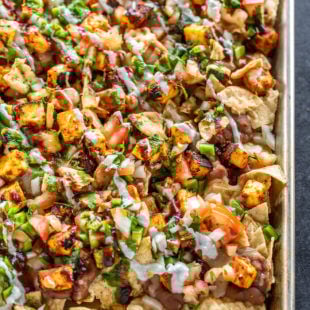 a full sheet of nachos topped with paneer, cheese, onion, tomato, cilantro
