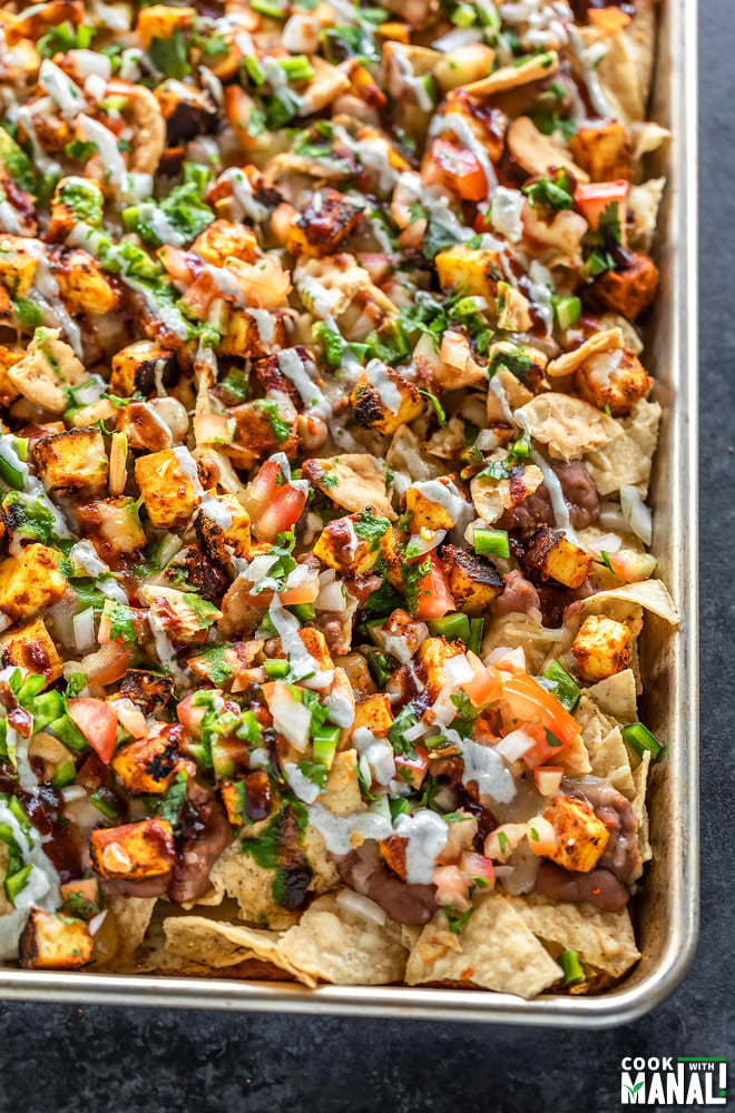 a full sheet of nachos topped with paneer, cheese, onion, tomato, cilantro