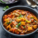 vegetable jalfrezi served in a black bowl with naan placed in the background along with some onion slices