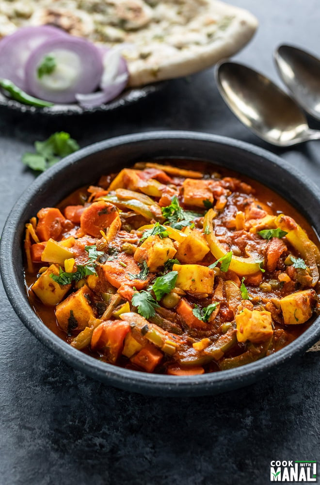 vegetable jalfrezi served in a black bowl with naan placed in the background along with some onion slices