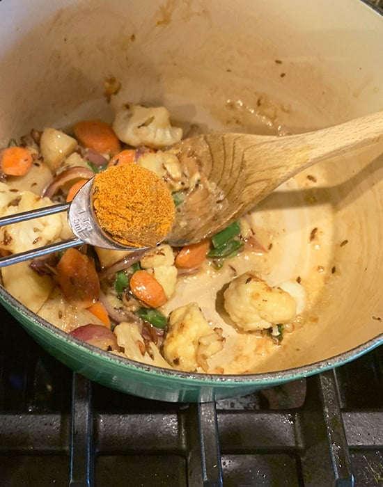 adding biryani masala to a pot using a spoon