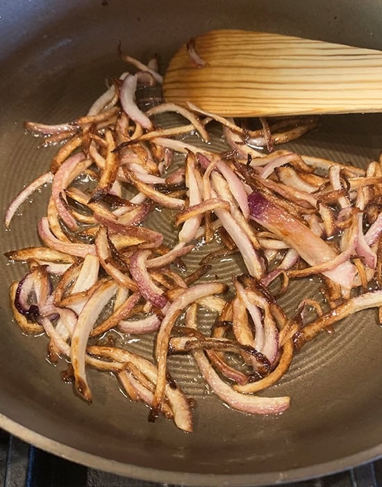 frying sliced onion in pan with a spatula