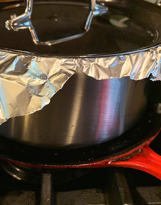 placing steel pot on top of a flat pan to cook the biryani