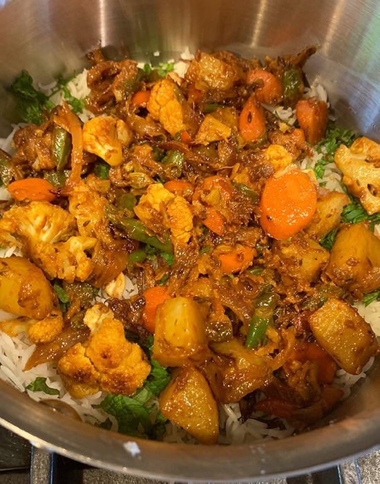 cooked vegetables layered on top of rice in a biryani pot