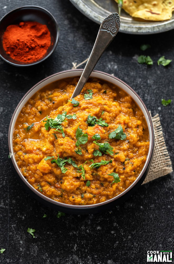 mashed butternut squash served in a black bowl with a spoon and garnished with cilantro