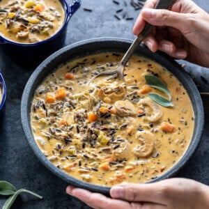 a pair of hands digging into a bowl of mushroom wild rice soup with a spoon