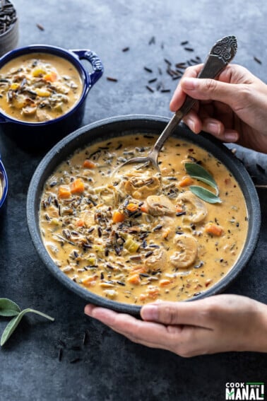 a pair of hands digging into a bowl of mushroom wild rice soup with a spoon