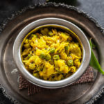 instant pot patta gobhi matar served in a small copper bowl and some curry leaves placed in the background