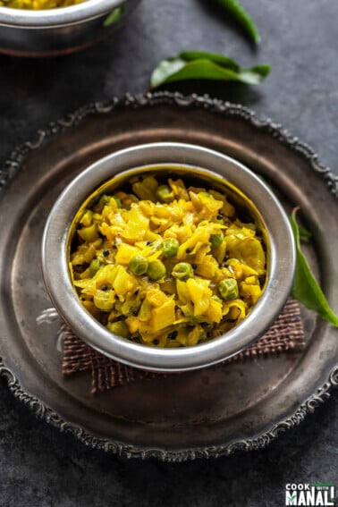 instant pot patta gobhi matar served in a small copper bowl and some curry leaves placed in the background