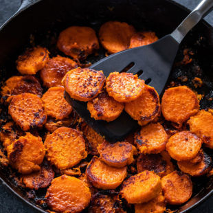 cast iron skillet with maple chili glazed sweet potatoes arranged in it