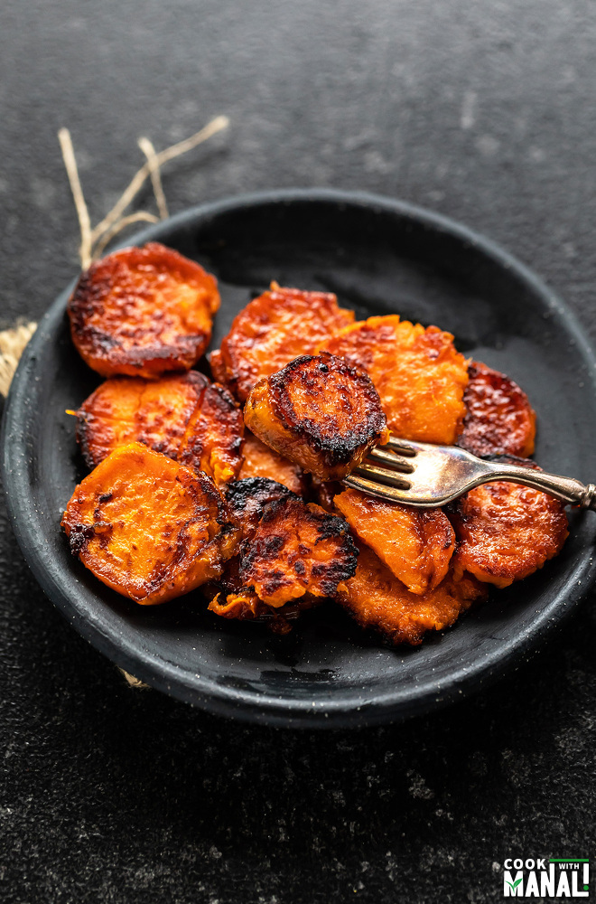 glazed sweet potatoes served in a black plate along with a fork
