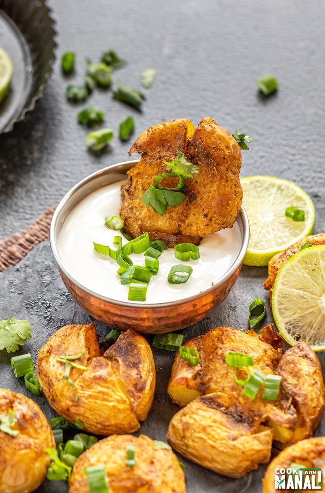 a masala smashed potatoes dipped into a bowl of sour cream
