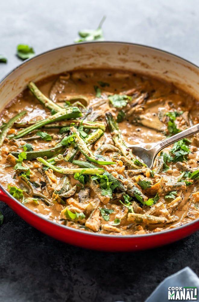 spoon dipping into a okra curry served in a red pan