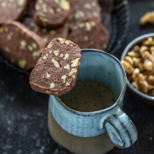 a chocolate walnut cookie placed on top of a coffee mug and a plate of cookies in the background