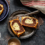 two slices of cake arranged in a plate with a fork and a cup of chai placed on the side