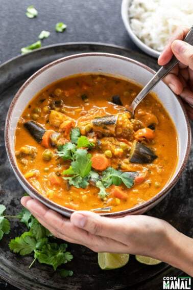 pair of hand holding a bowl of eggplant carrot curry