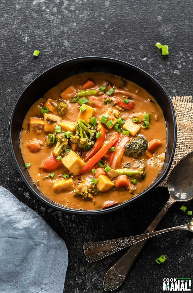 bowl full of veggies in peanut sauce with a blue color napkin placed on the side