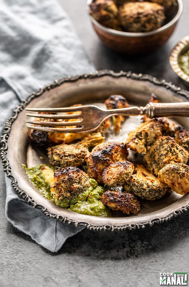 a roasted broccoli floret dipped in cilantro chutney with more roasted broccoli in the plate