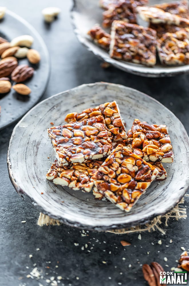 mixed nuts chikki in a white bowl and few nuts scattered on the sides and background