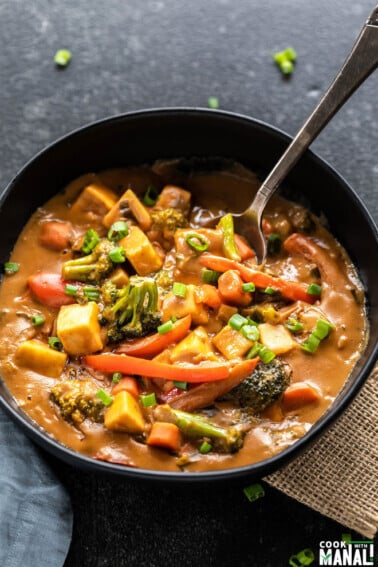 spoon digging into a black bowl of veggies in peanut sauce