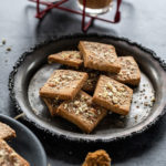 almond jaggery cookies placed in a silver plate with glasses of chai in the background