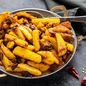 aloo bhujia (potato stir-fry) served in a copper plate with a grey color napkin in the background