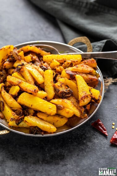 aloo bhujia (potato stir-fry) served in a copper plate with a grey color napkin in the background