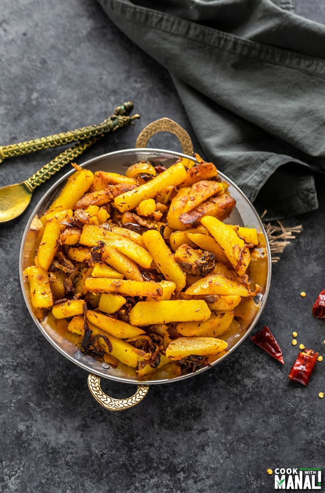 aloo bhujia sabzi served in a copper plate with two spoon placed on one side and a grey color napkin placed on the other side