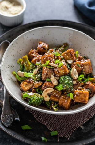 tofu broccoli stir-fry served in a white bowl with a spoon placed on the side