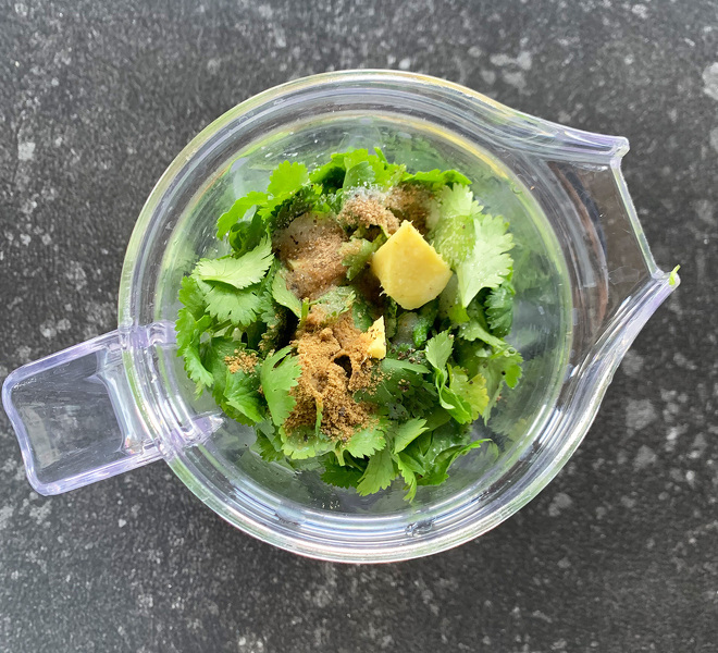 a blender with cilantro, ginger, chilies and spices added to it