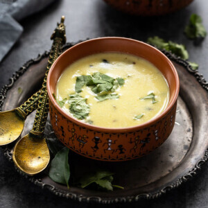 gujarati kadhi served in a ceramic bowl and garnished with cilantro with another bowl of rice in the background